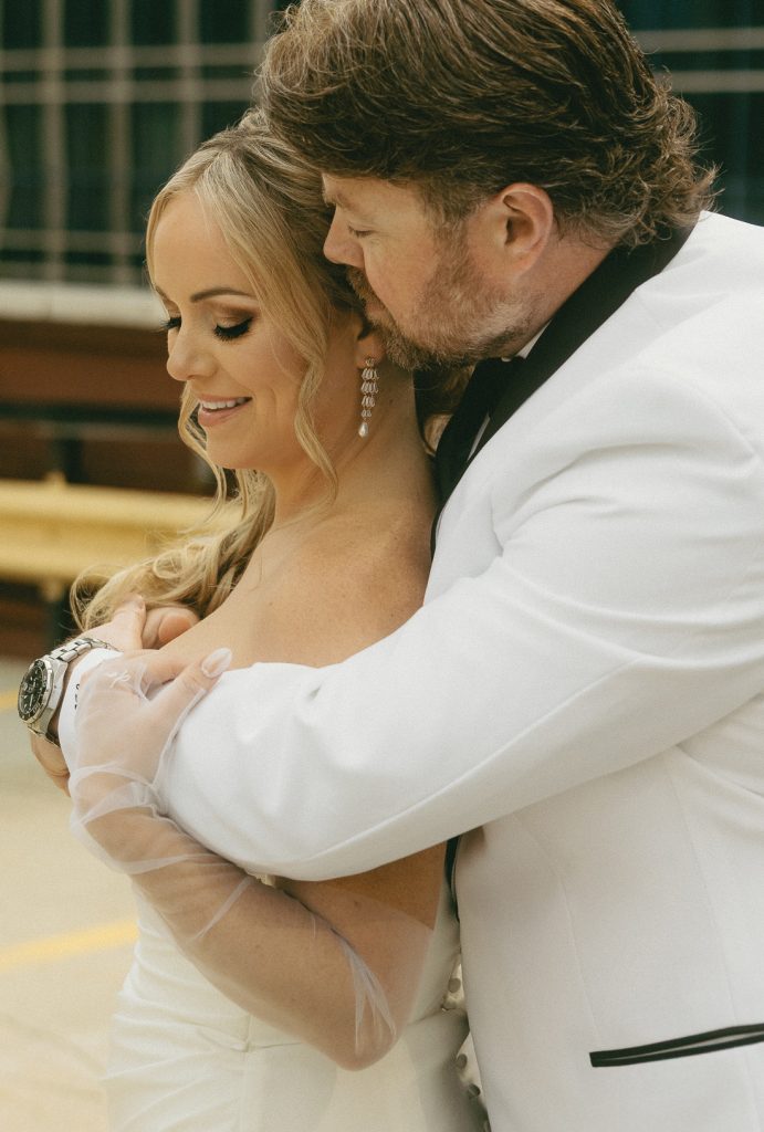 Lindsay and Cam Wedding-Joy By Joelle Portrait of groom in white tuxedo holding bride. Wedding design is by Joy By Joelle.